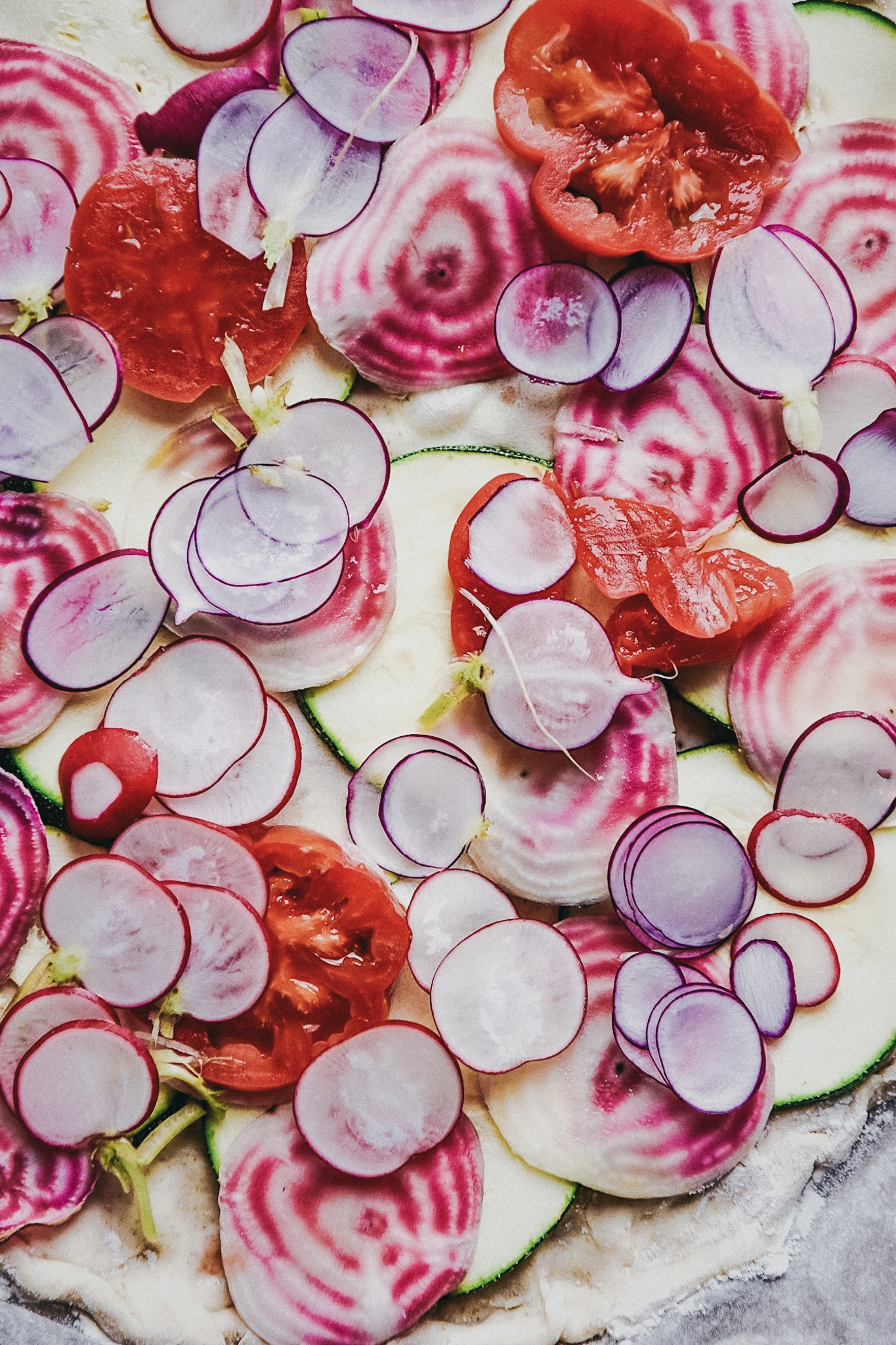 Plantbased pizza before baking with chioggia beets, radishes and zuchhini
