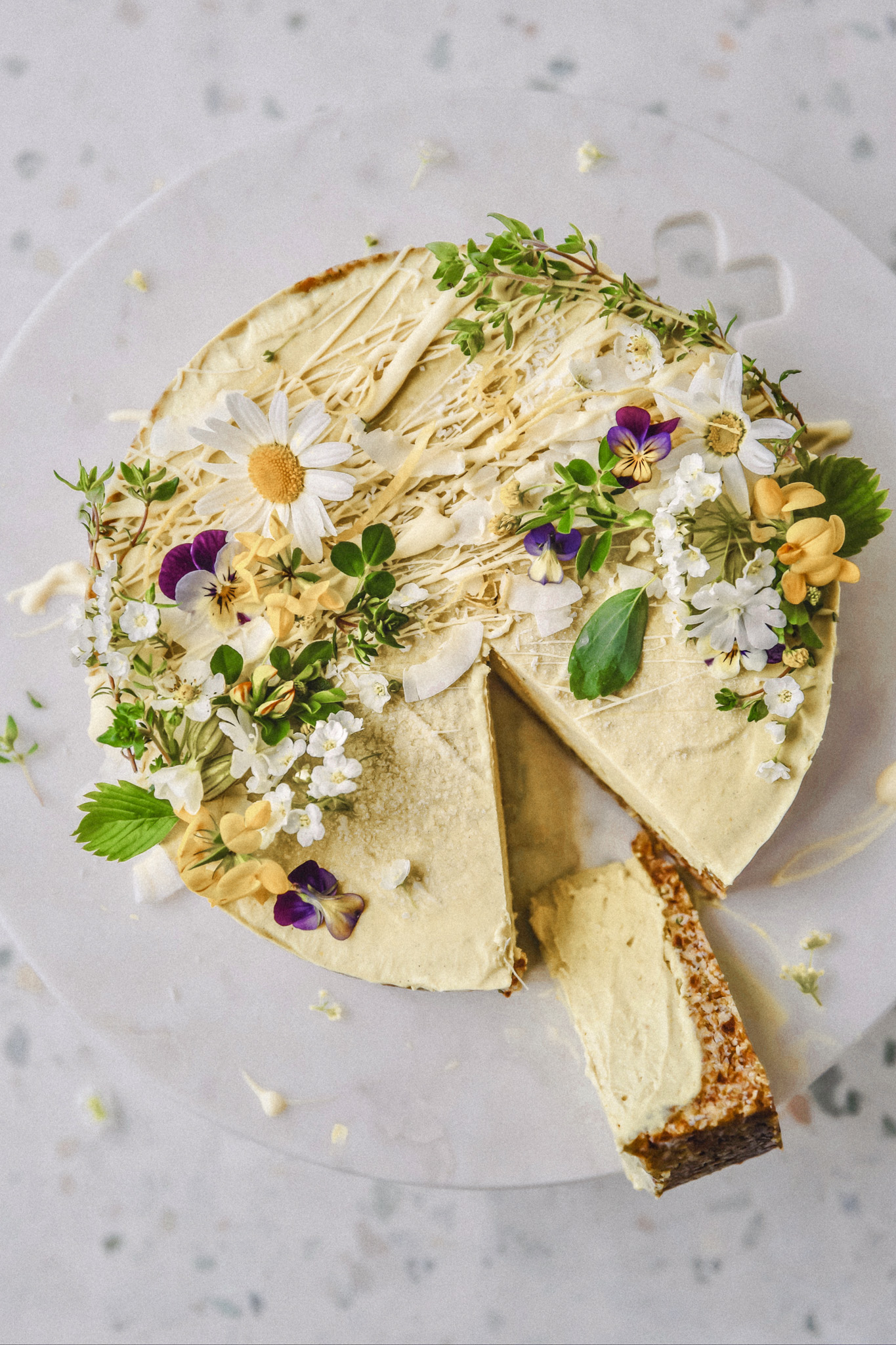 Raw lemon cake with edible blossoms on a marble plate