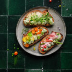 Sourdough toast with creamy herb dip and sliced veggies on a green tile background