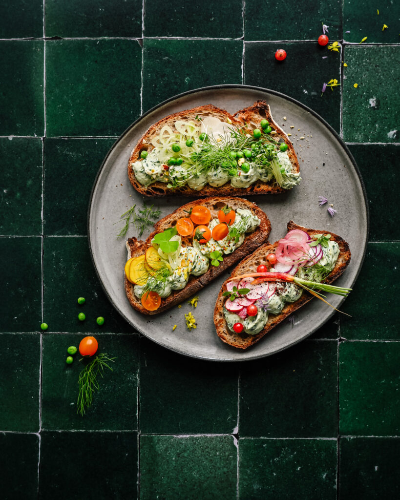 Sourdough toast with creamy herb dip and sliced veggies on a green tile background