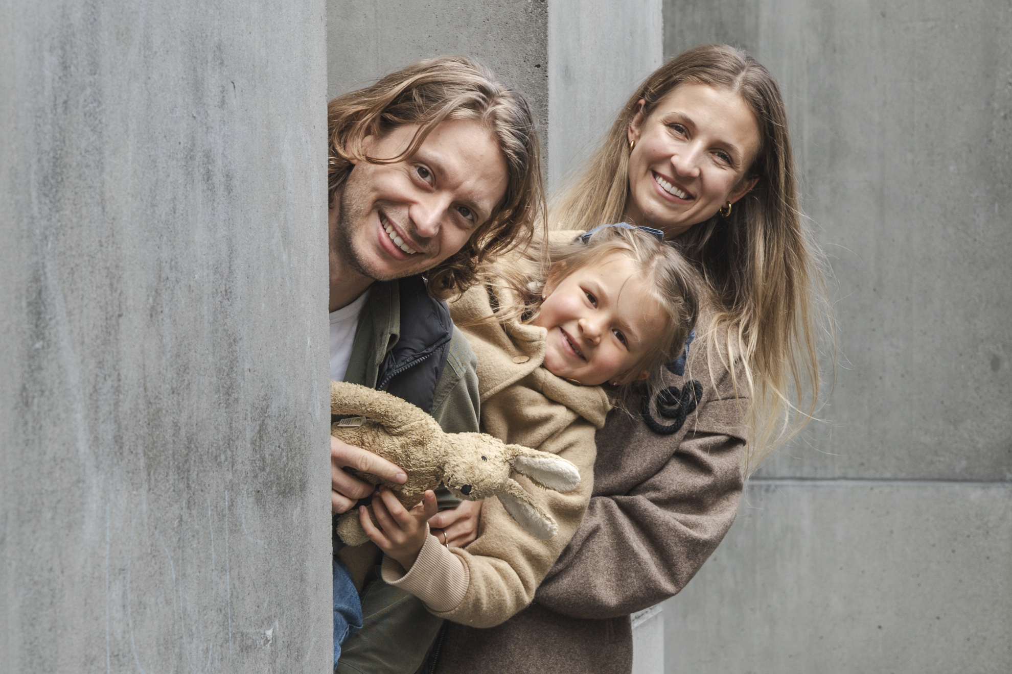 Cute family looking behind concrete pillars